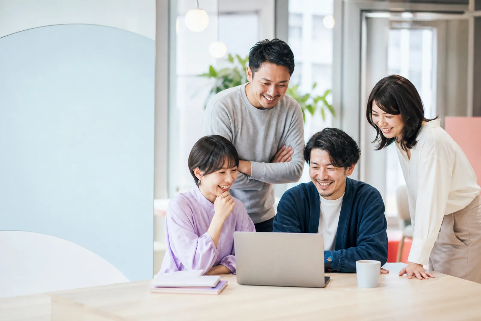 明るいオフィスで一緒に画面を見ながら働く4人のチーム